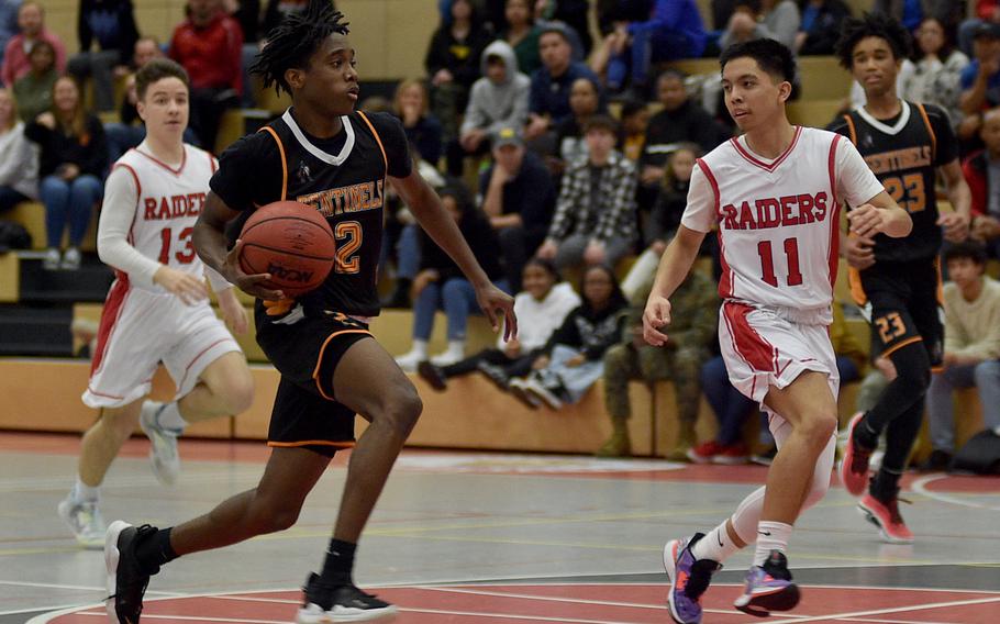 Spangdahlem's Makario Drummond drives to the basket as Kaiserslautern's Jayden Dayao gets back to defend during a game Friday evening at Kaiserslautern High School in Kaiserslautern, Germany. In the background, from left, are the Raiders' Logan Bell and the Sentinels' Robert Leggett.