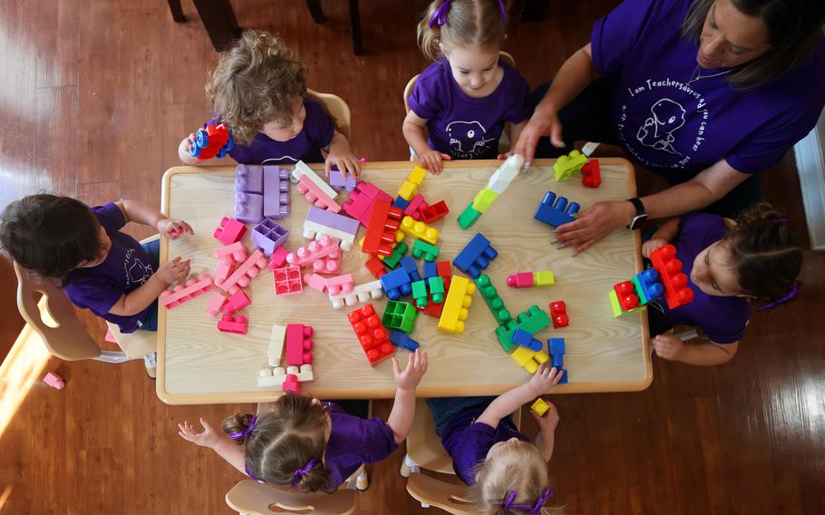An overhead view of children playing with puzzle blocks at a table with an adult.