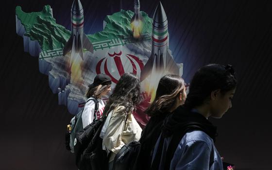 Iranian women walk past a banner showing missiles being launched in Tehran, Iran, on April 19, 2024.