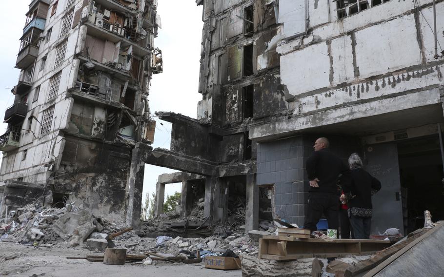 Local residents stand at the side of damaged during a heavy fighting buildings in Mariupol, in territory under the government of the Donetsk People’s Republic, eastern Ukraine, Friday, May 13, 2022. 