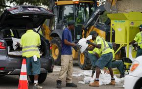 Eric Byrd hands a sandbag to Clifford Coston while working to fill people's trucks at a sandbag station at Northwest Park, Tuesday, Sept. 27, 2022, in St. Petersburg, Fla., as Hurricane Ian approaches. (Martha Asencia-Rhine/Tampa Bay Times via AP)