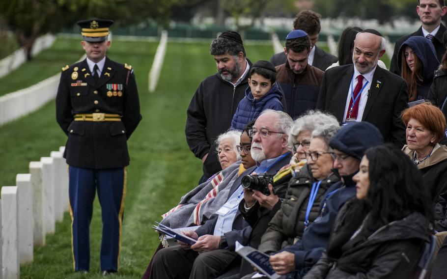 A row of people seated in front of tombstones while others stand behind them.