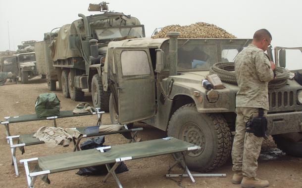 A soldier stands next to military truck in a convoy of vehicles.
