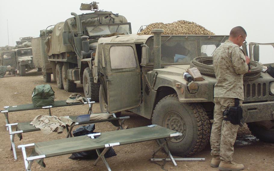 A soldier stands next to military truck in a convoy of vehicles.
