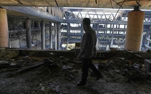 A man, seen from behind, walks in the upper levels of a damaged building as other damaged parts of the building are seen in the background.