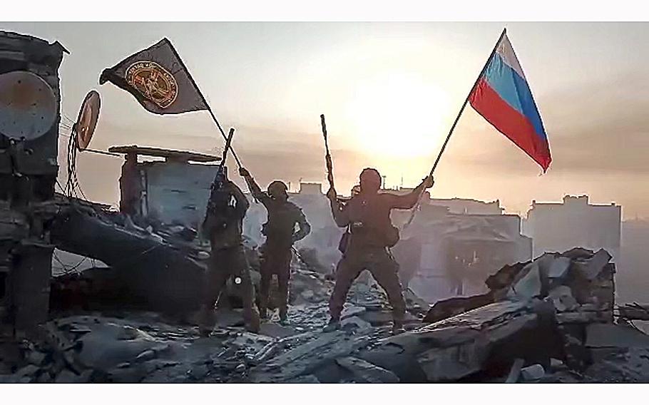 A screen grab from a video posted on May 20, 2023, shows Yevgeny Prigozhin’s Wagner Group military company members waving a Russian national and Wagner flag atop a damaged building in Bakhmut, Ukraine. 