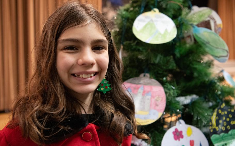 An elementary schooler smiles in front of a Christmas tree.