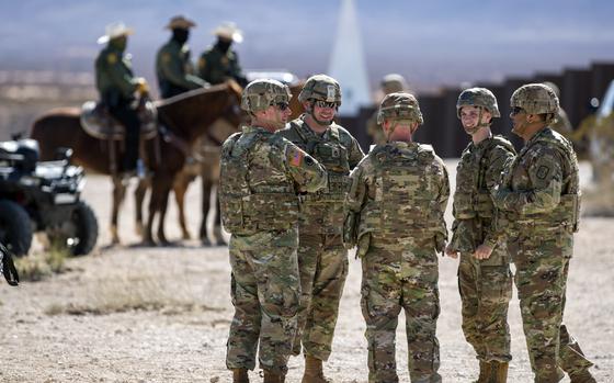Army soldiers chat while standing in the desert.