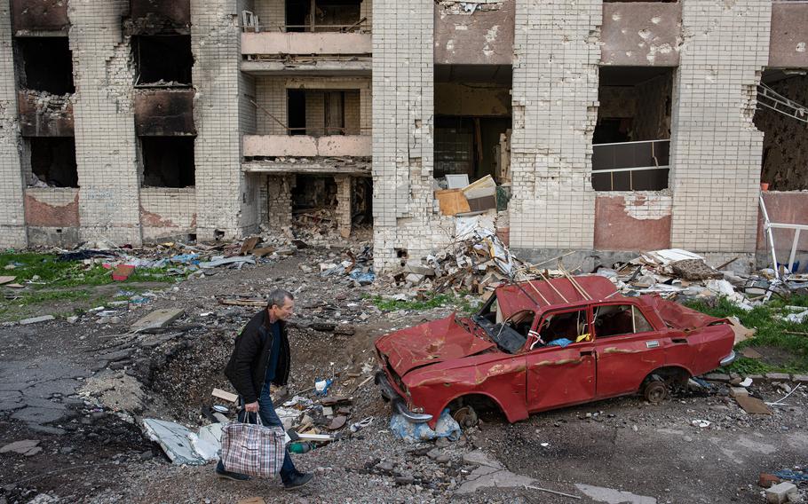 A man carries his belongings past a destroyed car next to a heavily damaged apartment building on May 28, 2022, in Chernihiv, Ukraine.