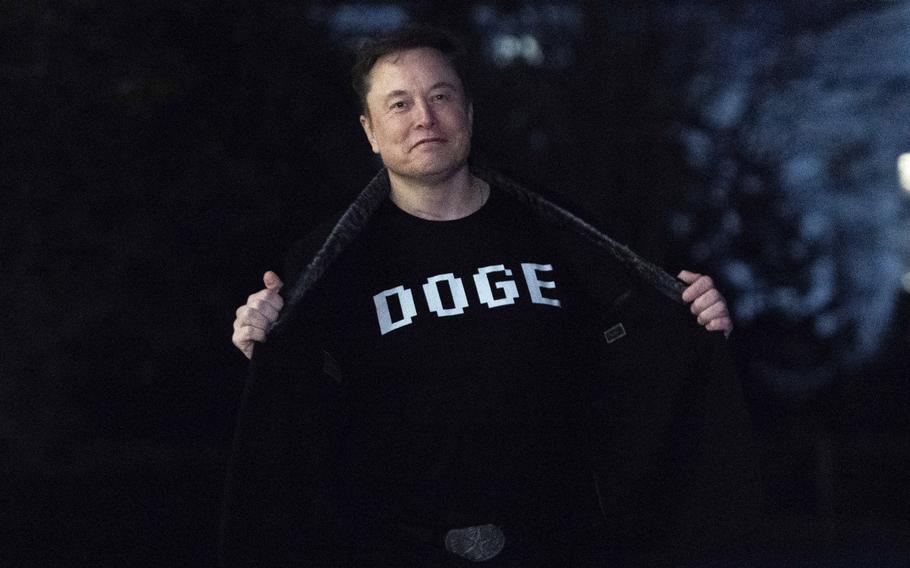 Elon Musk holding open a jacket to reveal his shirt with the name of his government agency emblazoned on it.