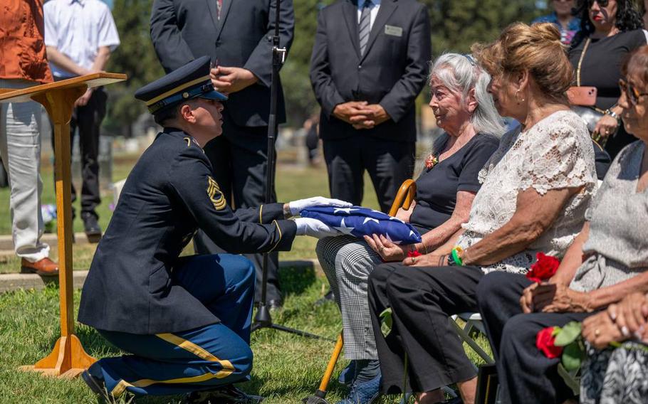 A kneeling soldier presents a folded American flag to an elderly woman.