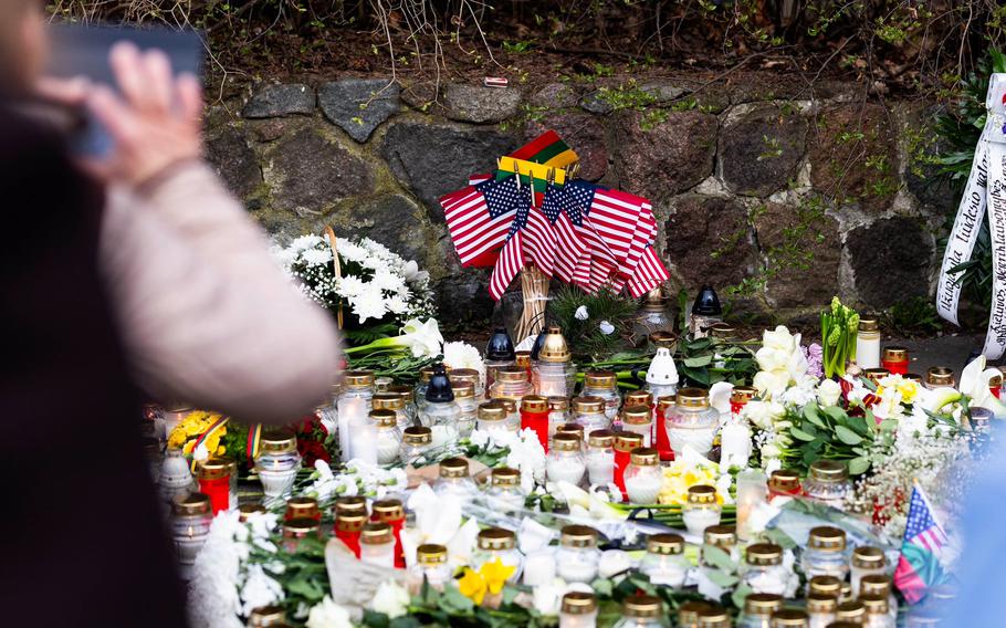 A person photographs the memorial of candles, flowers and U.S. flags.