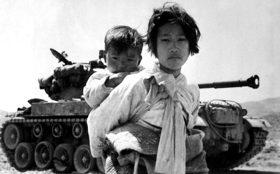 With her brother on her back, a Korean girl tiredly trudges by a stalled M-26 tank in Haengju, Korea, June 9, 1951.  