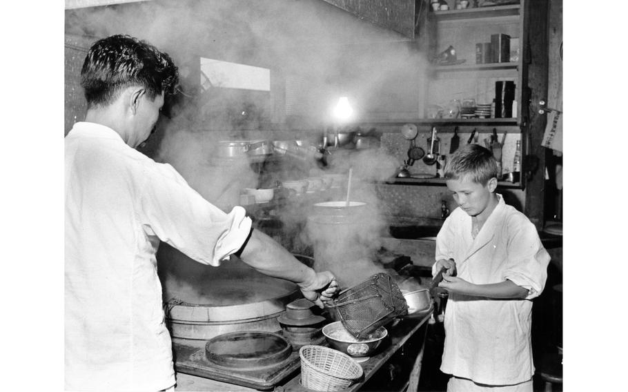 A child cooks noodles with a Japanese man in a kitchen