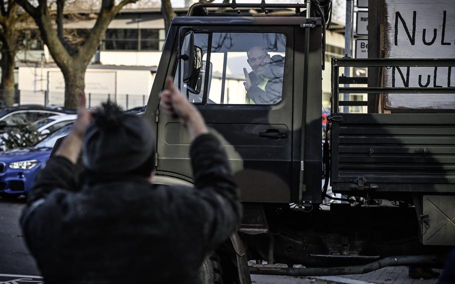 An onlooker cheers for a driver of an old German military vehicle participating in a farmers protest in Kaiserslautern, Germany, Jan. 8, 2024. The vehicle's hand-painted poster criticizes the German government as "clueless."