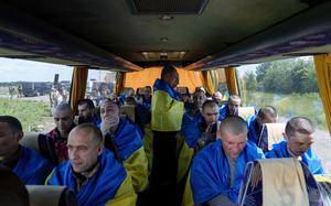 Ukrainian soldiers wearing Ukrainian flags sit in a bus.