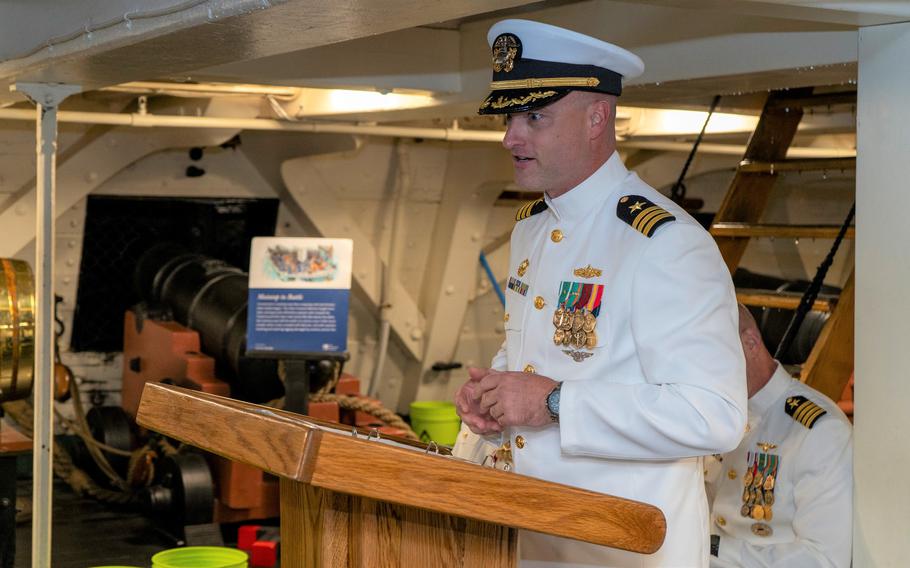 A man in a white Naval uniform stands at a podium.