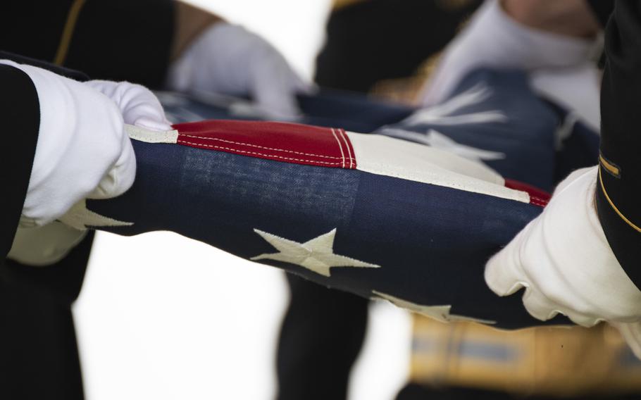 U.S. Army soldier wearing white gloves fold an American flag at a military funeral.