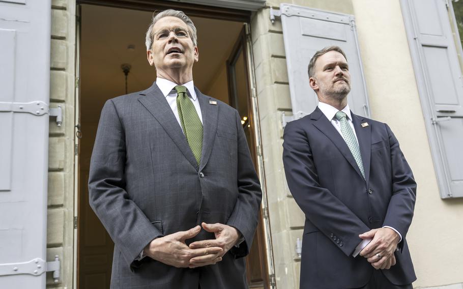 Bessent and Greer stand outside the door with their hands crossed at their waists.