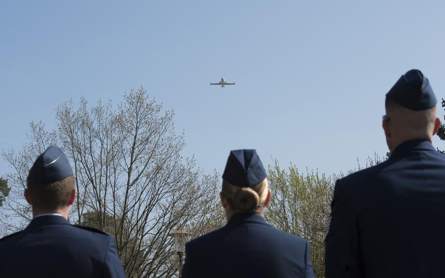 Three airmen wearing service dress uniforms watch a plane fly overhead.