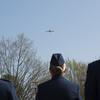 Three airmen wearing service dress uniforms watch a plane fly overhead.