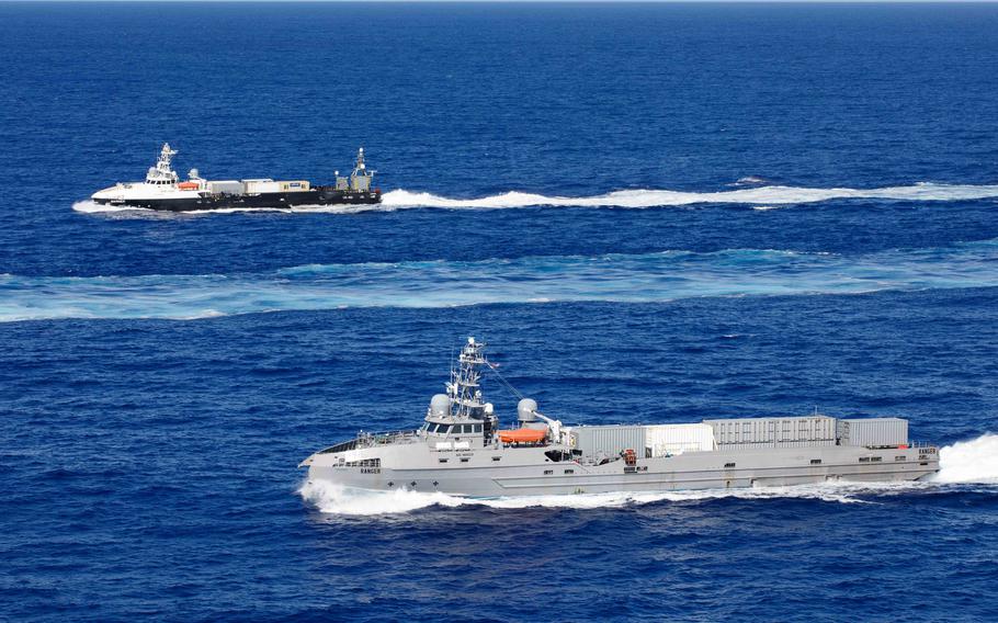 Two military vessels operate in deep blue ocean waters. 