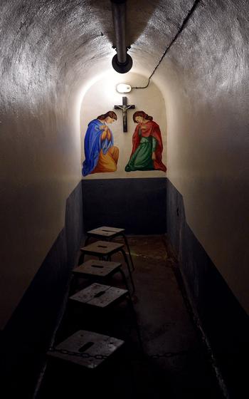 Underground chapel or religious space with arched ceiling, featuring a painted scene with Mary and Joseph kneeling with a crucifix mounted above.