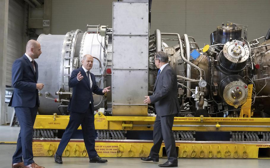 German Chancellor Olaf Scholz, center, gestures besides Christian Bruch, CEO of Siemens Energy, left, at the turbine serviced in Canada for the Nordstream 1 natural gas pipeline in Muelheim an der Ruhr, Germany, Aug. 3, 2022. 