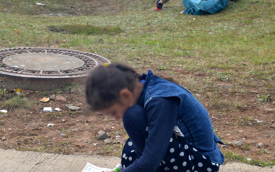 An Afghan girl draws while two boys play on the grass at Rhine Ordnance Barracks in Kaiserslautern, Germany, Aug. 30, 2021. More than 3,000 evacuees from Afghanistan have been housed at the Army installation, which is taking some of the pressure off Ramstein Air Base, where around 24,000 evacuees have arrived in the past two weeks.