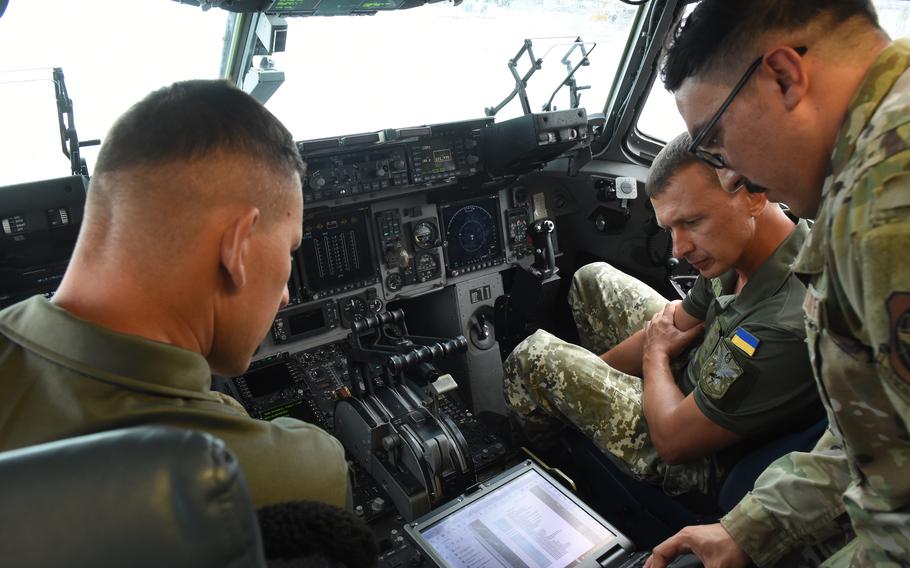 Staff Sgt. A.J. Juarez, a C-17 and C-5 crew chief, shows Capts. Volodymyr Bren, right, and Volodymyr Shkrobtak, Ukraine air force air traffic controllers, an operations manual for the C-17 inside the cockpit during a tour of the aircraft on Aug. 5, 2021, at Ramstein Air Base, Germany. 