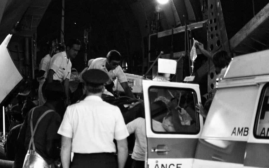 In this black and white photo, many people surround an ambulance.