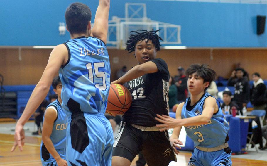 Zama's Casey Stewart goes up between Osan's Ben Ziegler and Jax Ibarra. The Trojans won 59-26.