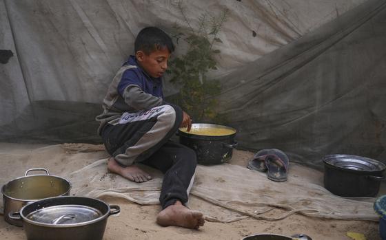 A barefoot child sits next to a pot of food.
