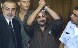 FILE - Marwan Barghouti, center, raises his handcuffed hands in the air on the opening day of his trial at Tel Aviv's District Court on Aug. 14, 2002. Hamas officials say that any cease-fire deal with Israel should include the release of prisoner Marwan Barghouti — a leader of the militant group's main political rival. The demand by Hamas marks the central role Barghouti plays in Palestinian politics — even after more than two decades behind bars and sentenced by Israel to multiple life terms in prison. (AP Photo/Brennan Linsley, File)