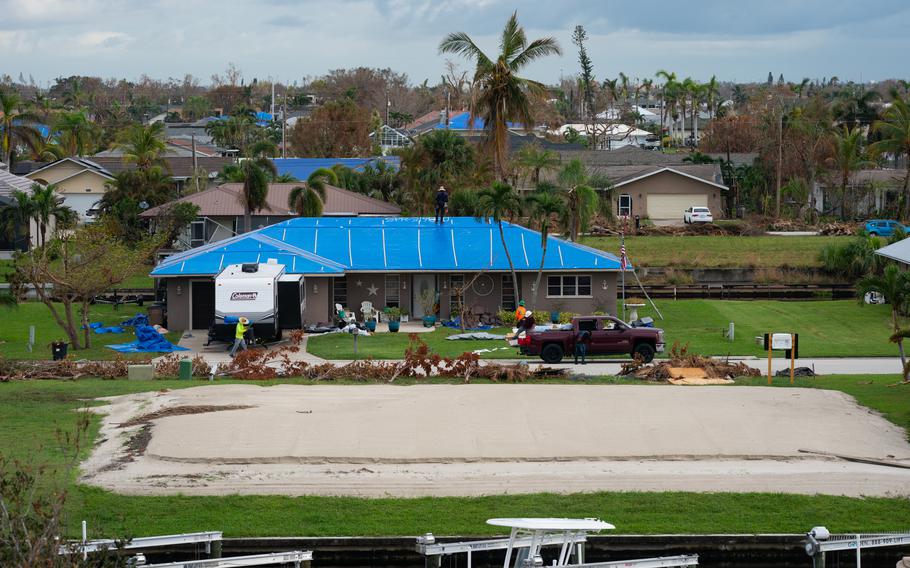 Workers cover a damaged roof with a tarp.