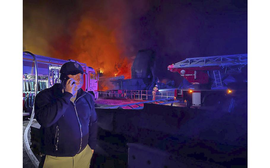 Sevastopol Gov. Mikhail Razvozhaev speaks on a mobile phone as smoke and flame rise from a burning Sevastopol Shipyard in Crimea on Sept. 13, 2023.