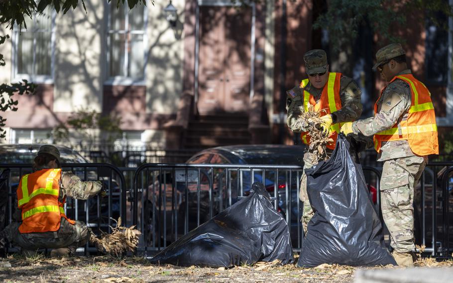Three soldiers wearing orange vests over their military uniforms, picking up trash.