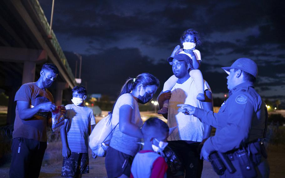 A Venezuelan family is instructed by a Border Patrol officer near the Eagle Pass-Piedras Negras International Bridge shortly after crossing the Rio Grande on Aug. 12, 2022.