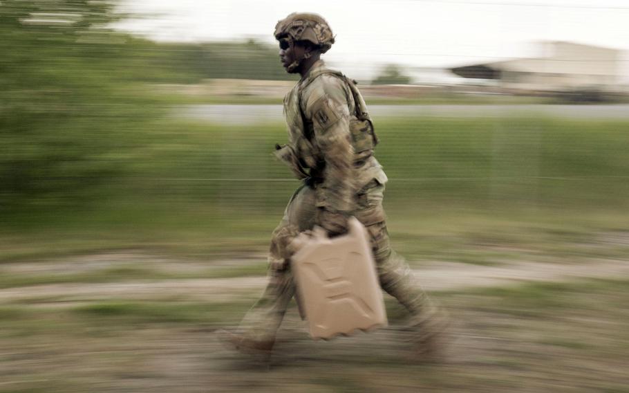 A soldier runs or speed walks with a jerry can; his surroundings are blurred.