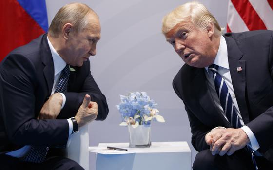 Vladimir Putin and Donald Trump lean to their sides as they speak while seated next to one another.