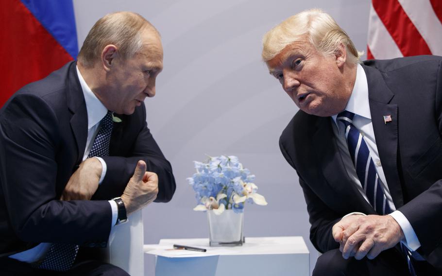 Vladimir Putin and Donald Trump lean to their sides as they speak while seated next to one another.