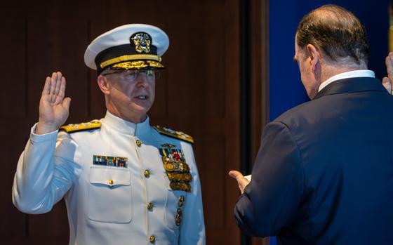A Navy officer in white dress uniform and hat takes an oath of office with his right hand raised.