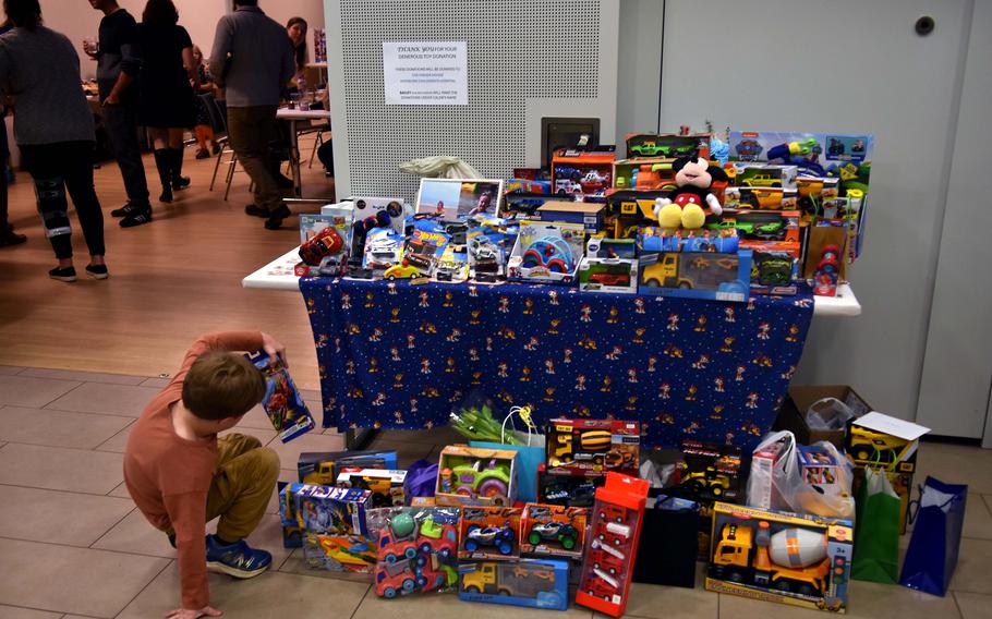 A boy picks up a toy in front of a table holding cars, trucks, a stuffed Mickey Mouse and other toys donated in memory of Caleb Anders.