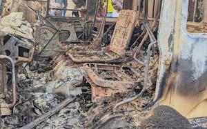 A burned-out vehicle, with people looking through the windows.