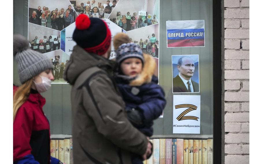 A family walk past a portrait of Russian President Vladimir Putin, a sign reading 'Go Russia!' and the letter Z, which has become a symbol of the Russian military, displayed in the window of a children's library in St. Petersburg, Russia, on March 11, 2022. 