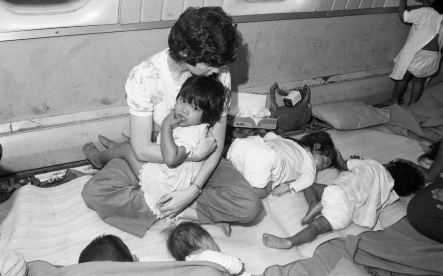 A woman holds a toddler in her lap while several infants sleep around her.
