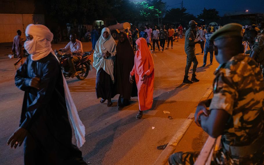 People walk past the military forces and the National Police at the Rond-Point de l’Escadrille in Niamey.