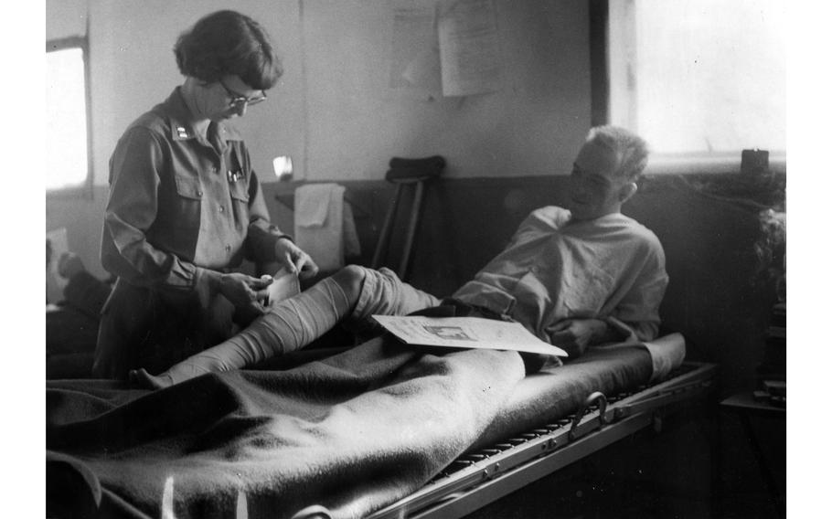 Capt. Virginia Brown, chief nurse at the quonset hut hospital adjecent to the 54th Medical Detachment’s air ambulance helicopter field, adjusts the leg bandage of a wounded soldier. 