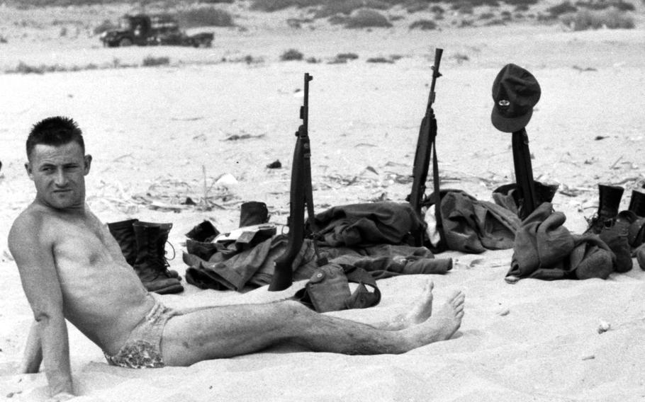 An American soldier from Army Task Force 201 warily relaxes on a Beirut beach as his fellow troops swim in the Mediterranean during the American intervention in Lebanon. The troops wore full combat dress on the more than two-mile march from the bivouac area to the isolated, mile-long swimming area.