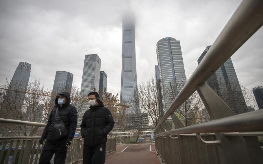 Commuters wearing face masks to protect against COVID-19 walk across a pedestrian bridge in the central business district in Beijing, Thursday, Dec. 23, 2021. 